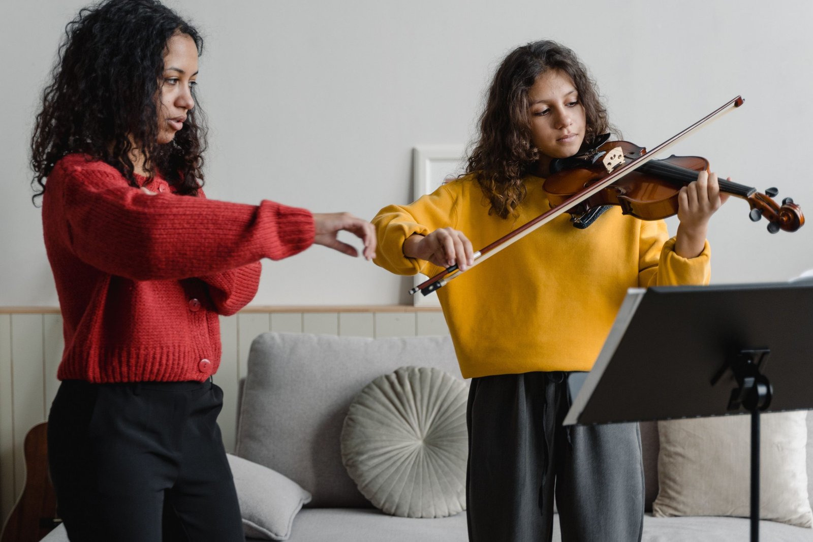 Teenage girl receiving violin lesson from female instructor indoors.